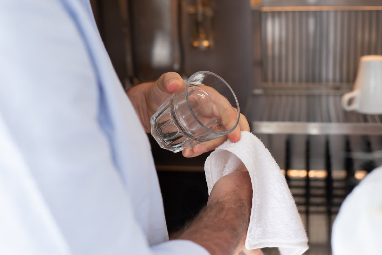 services-04 A person drying a glass with a towel in an indoor kitchen setting.